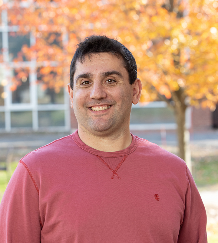 Steve smiling outside in front of a tree with orange leaves